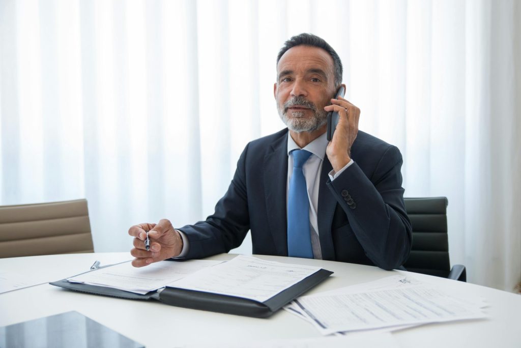 Senior businessman in suit discussing important documents on the phone at an office room.